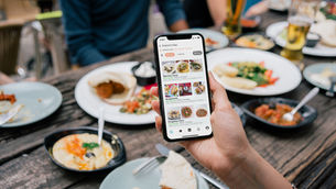 Ein Smartphone mit dem Menü eines Restaurants auf dem Bildschirm, gehalten vor einem gedeckten Tisch.