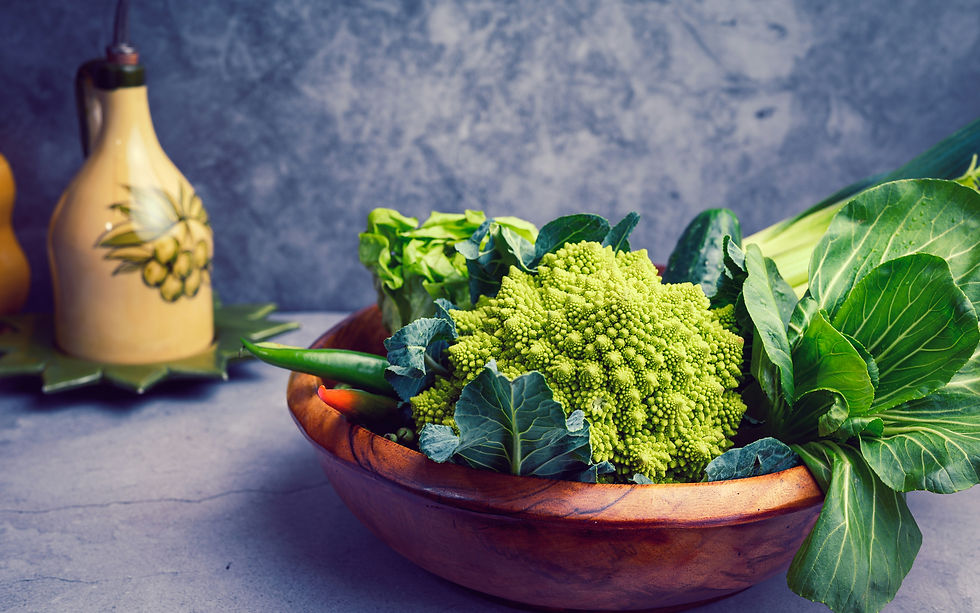 Wooden bowl with romanesco, lettuce, and greens on a gray counter. Olive oil bottle with a fruit design in the background.