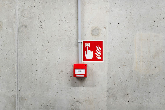 Red fire alarm switch on a concrete wall with a sign showing a hand pressing a button and flames