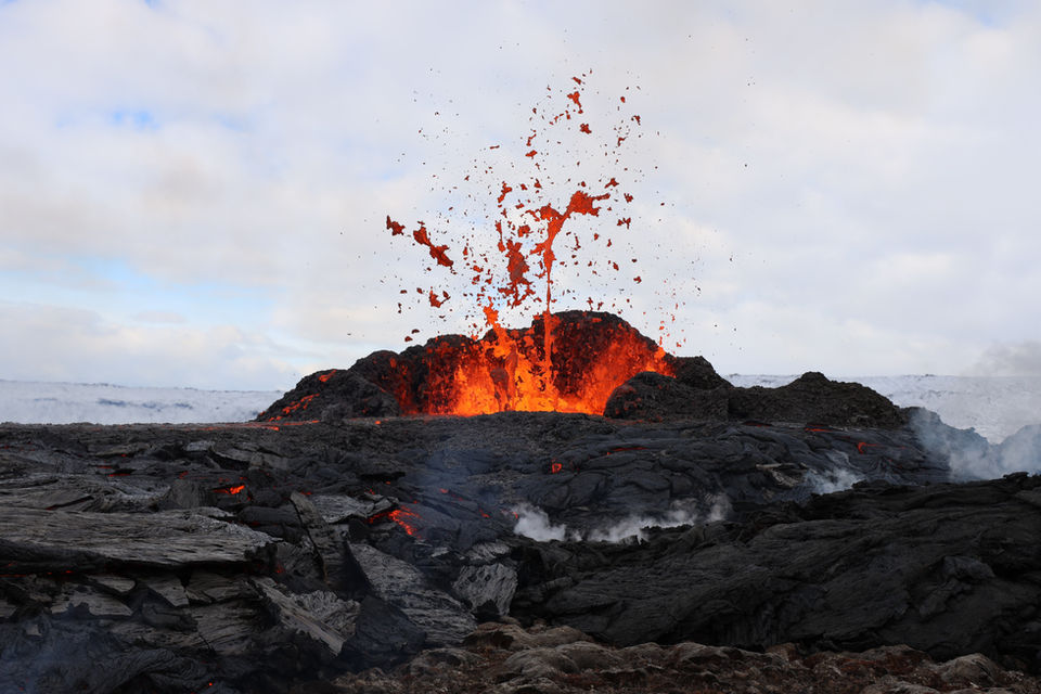 Esplosione di lava da un cratere vulcanico in Islanda con fumo e cielo coperto