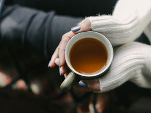 A woman's hands holding a cup of tea, in a cozy setting for some reflection and healing time.