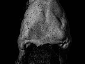 Muscular back in push-up position, black and white. Dark hair, textured skin, and strong shadows against a black background.