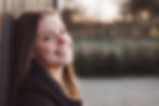 Smiling young woman leaning against a fence outdoors at sunset, with a blurred park background and warm light.