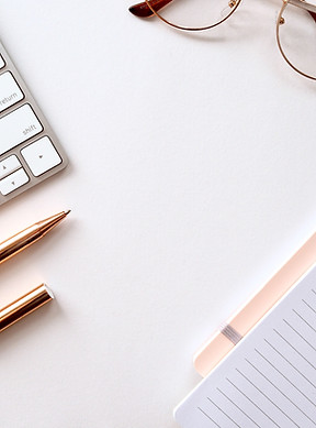 Zoomed in picture of a keyboard, pen, glasses and notepad