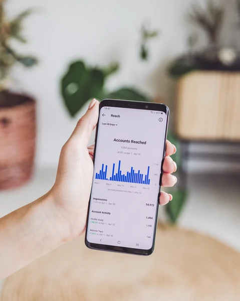 a hand holding a phone, on the screen is Instagram's analytics, accounts reached page