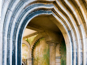 Ornate stone archway with columns and patterned grooves. Background wall has green moss stains. No text or people visible. Calm ambiance.