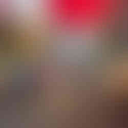 Tourists and locals walking through the vibrant, sun-drenched main thoroughfare of the Carmel Market under colorful red awnings.
