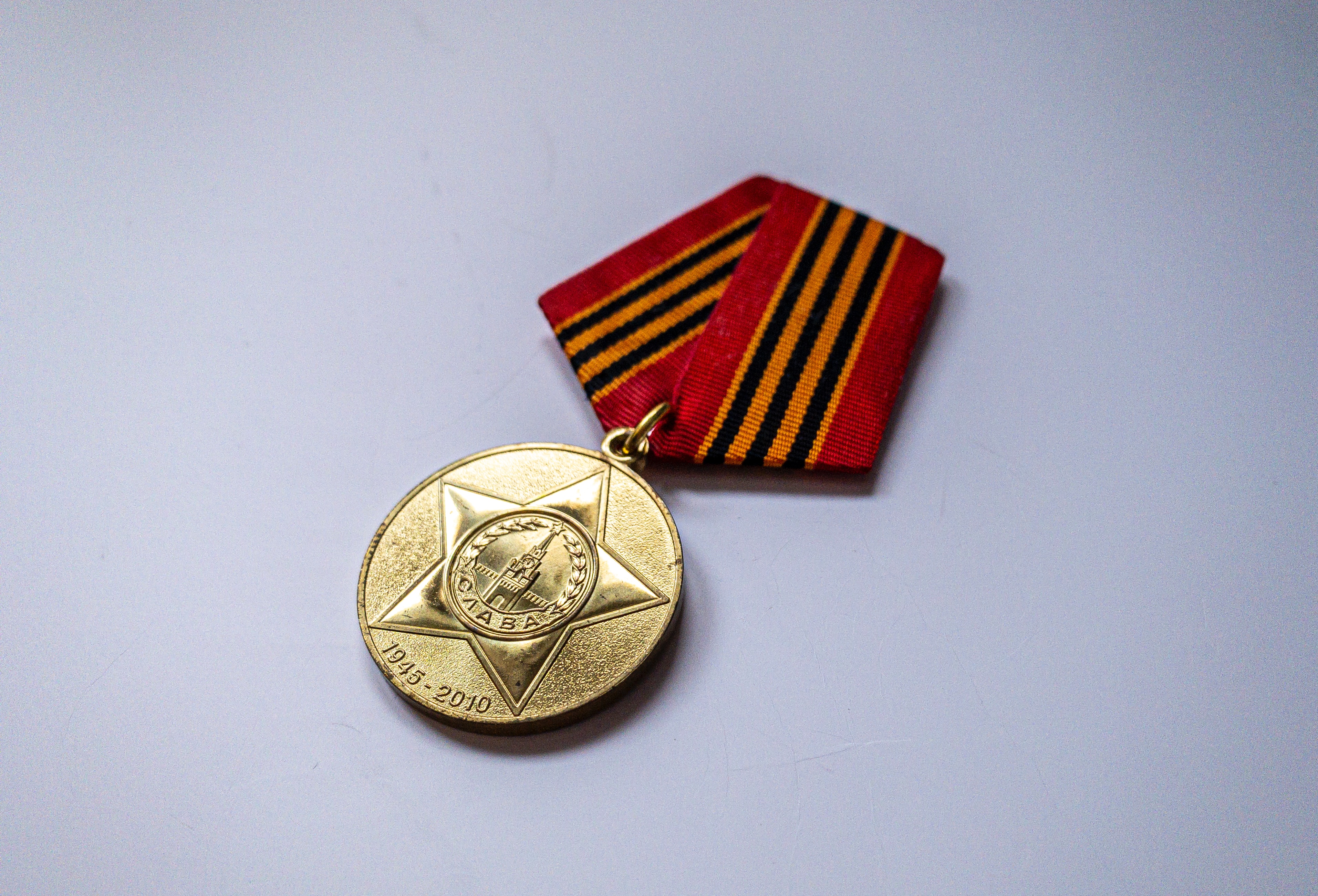 A 3D stylized gold medal with an engraved star hanging from a red and orange striped ribbon.
