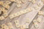Scrabble tiles spelling "HEALTHY" on a wooden surface, surrounded by scattered letters. Warm tones and a casual atmosphere.