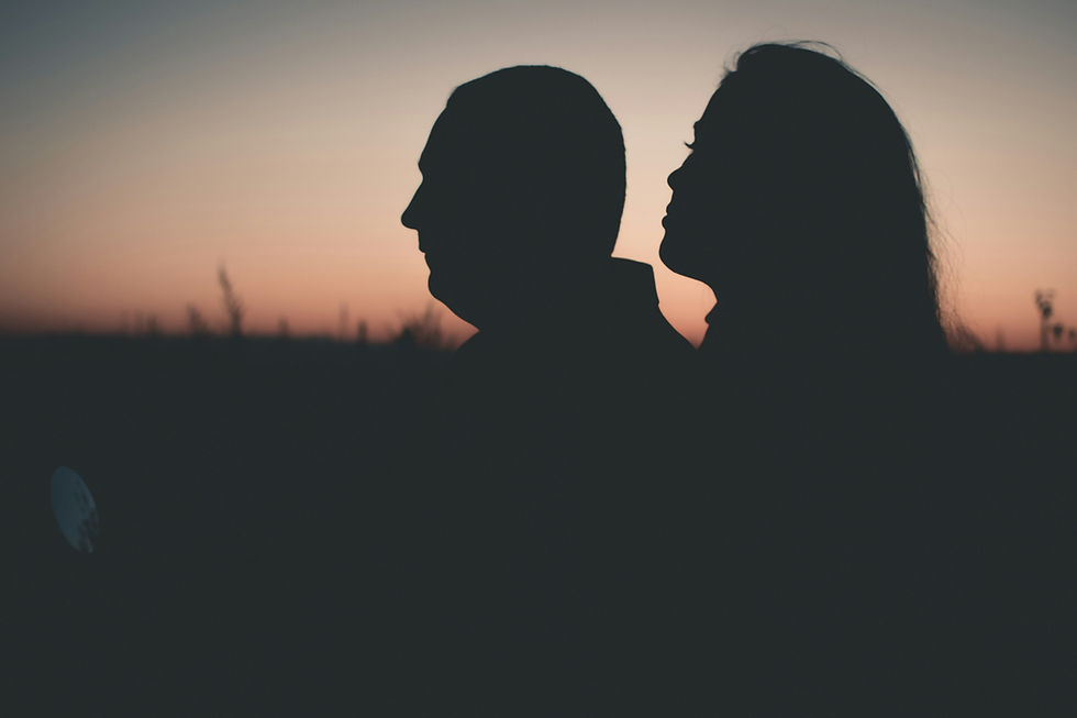 Silhouetted profiles of two people against a sunset sky, creating a serene mood. The sky features shades of orange and pink.
