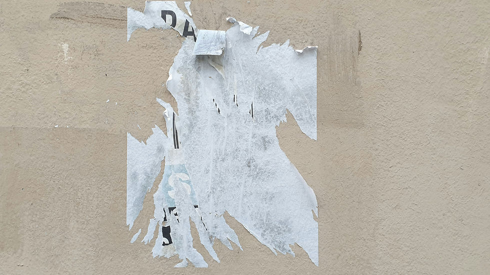 Torn white poster scraps on a beige wall, with partial black letters visible and a worn, weathered look.