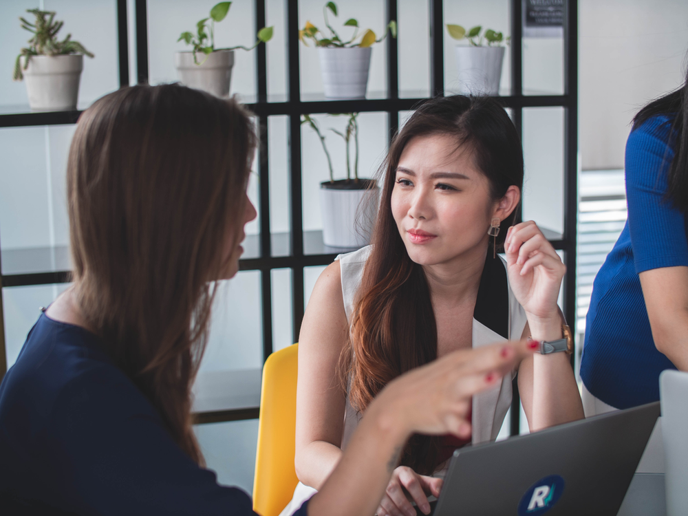 A woman demonstrating active listening during a meeting by looking at the speaker rather than at her laptop.