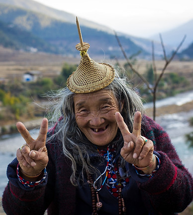 Portrait of an elderly Bhutanese woman smiling warmly at the camera, her face lined with wisdom and experience, dressed in traditional attire with vibrant patterns, capturing the charm and spirit of Bhutanese culture