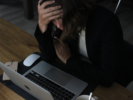 mulher no computador com cara de preocupada olhando para a tela e com a mão na testa.