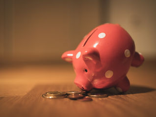 Pink polka-dot piggy bank tipped over on a wooden floor with coins spilling out in warm light.