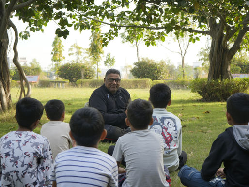 Man seated outside facing group of seated younger students in outdoor setting