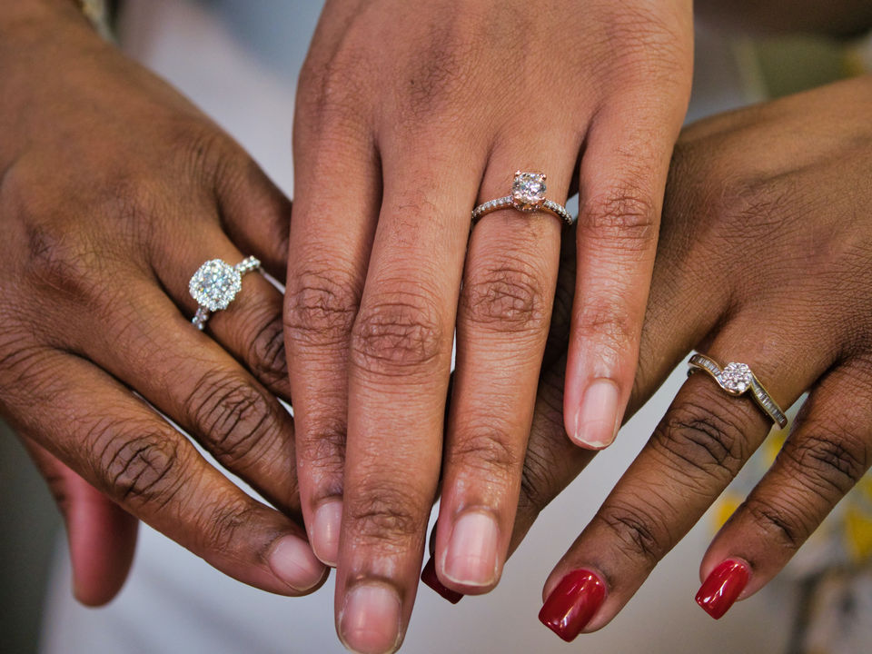 Three women showing their diamond rings, featuring round brilliant cut diamonds and large solitaire diamonds, in yellow gold.