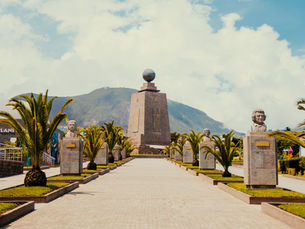 Mitad del Mundo monument near Quito, Ecuador, framed by palm trees and the Andes.