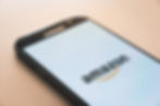 Samsung phone displaying Amazon logo on a white screen, placed on a light surface. Calm and modern tech vibe.