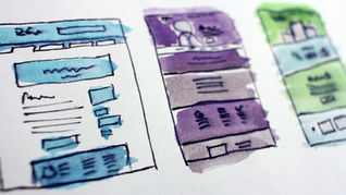 Three colorful website wireframes with blue, purple, and green accents on paper. Abstract and artistic design with handwritten elements.