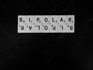 White Scrabble tiles spell "BIPOLAR" against a black background. The word is mirrored below, creating a reflective and balanced effect.