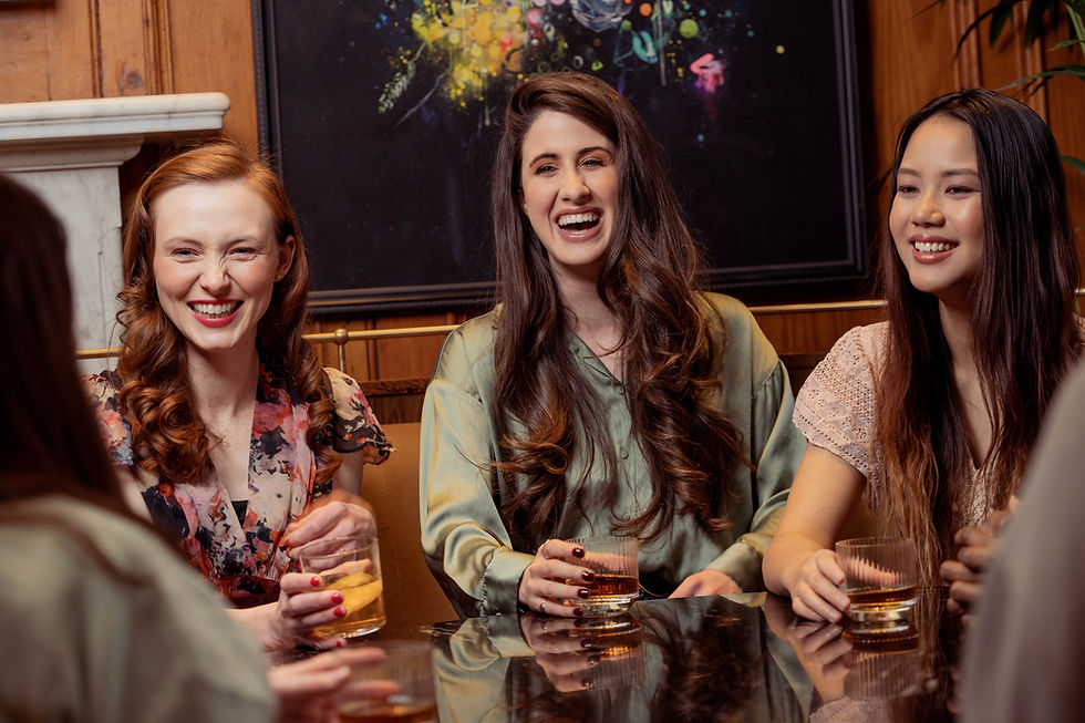 three women enjoying drinks together in a group setting and laughing