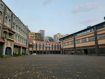 View of a traditional school building with an open courtyard, surrounded by multiple school blocks and a few fallen leaves on the ground.