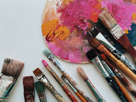 Paint-smeared palette with colorful brushes arranged on a white surface, a creative art workspace with pink, orange, and blue tones