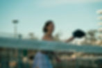 Smiling woman plays pickleball outdoors at dusk, holding a black paddle on a blurred court with a pale blue sky.