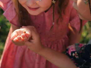 A young child gently holding a tiny ladybug while exploring nature with a caring adult nearby.