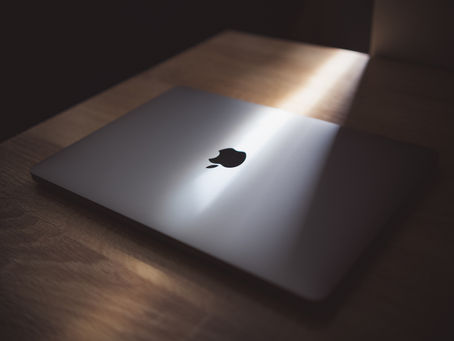 Closed laptop with Apple logo, on a wooden table. A beam of light highlights the logo, casting a calm, minimalist ambiance.