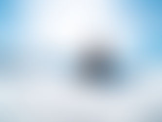 A girl at the top of the mountain wearing snowboarding gear, the sun behind her.