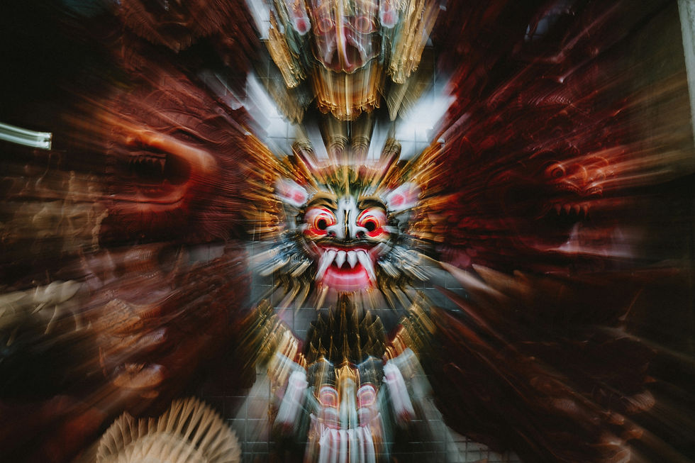 Blurred close-up of ornate red, gold, and white demon masks on a wall, creating a dramatic swirling effect