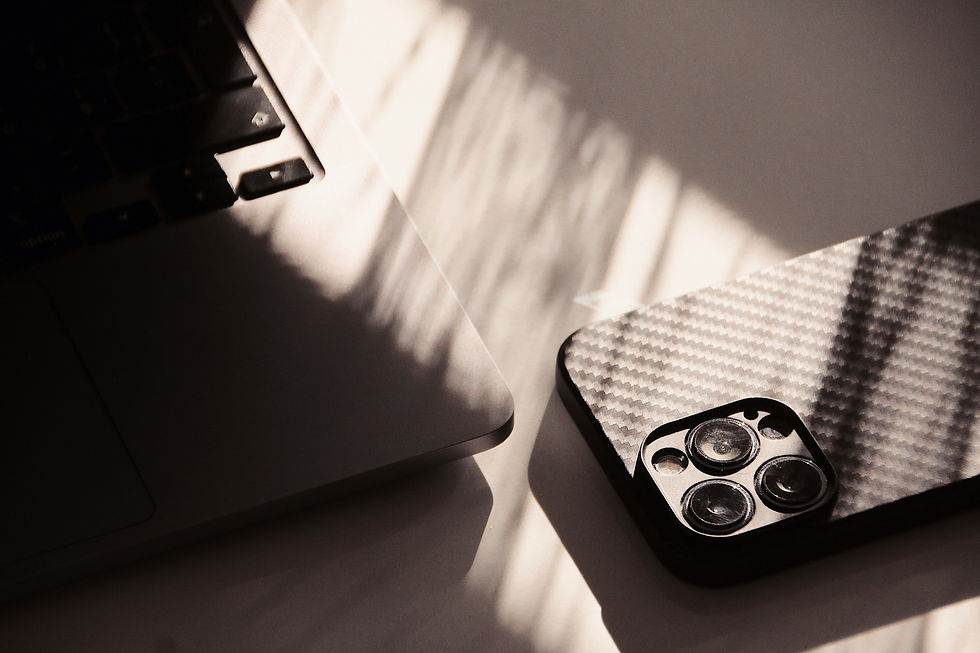 Two smartphones on a sunlit table, one matte black and one carbon-fiber, with soft window shadows.