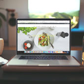 Photo of an open laptop on a table with a small cactus, a water bottle, and a newspaper