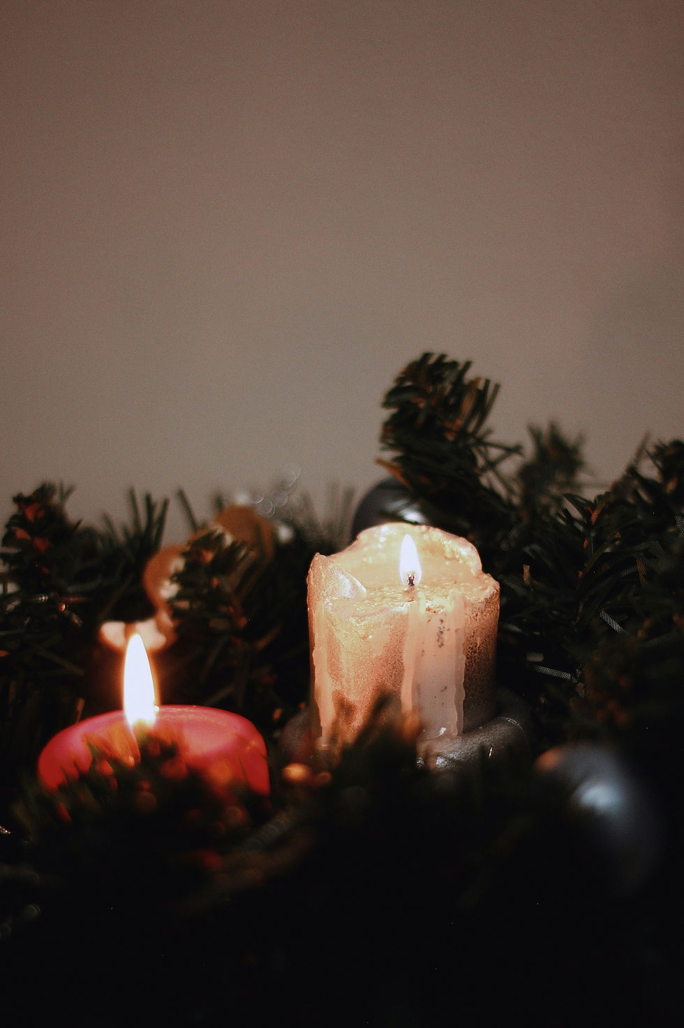 An image of a red candles and white candle lit, burning among tinsel