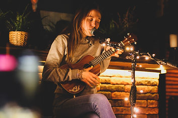 Female ukulele-playing teen performing at night with fairy lights