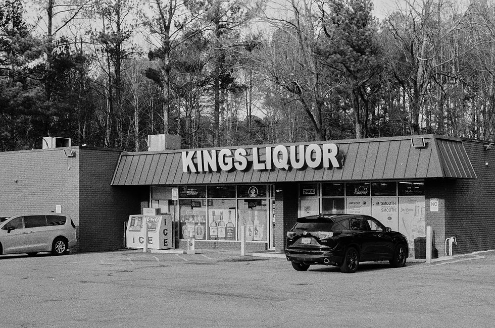 Kings Liquor store with two parked cars in front. Forest background. Signage visible. Black and white photo. Calm atmosphere.