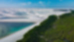 Huge field of white sand dunes filled with turquoise blue water meets a green forest