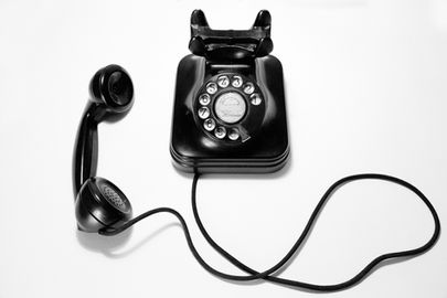 An old fashioned black phone with cable and circular dial.
