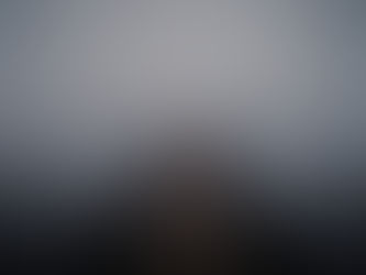 Wooden pier extends into foggy, serene lake. Bare branches frame the edges. Moody, muted blues and grays dominate the misty scene.