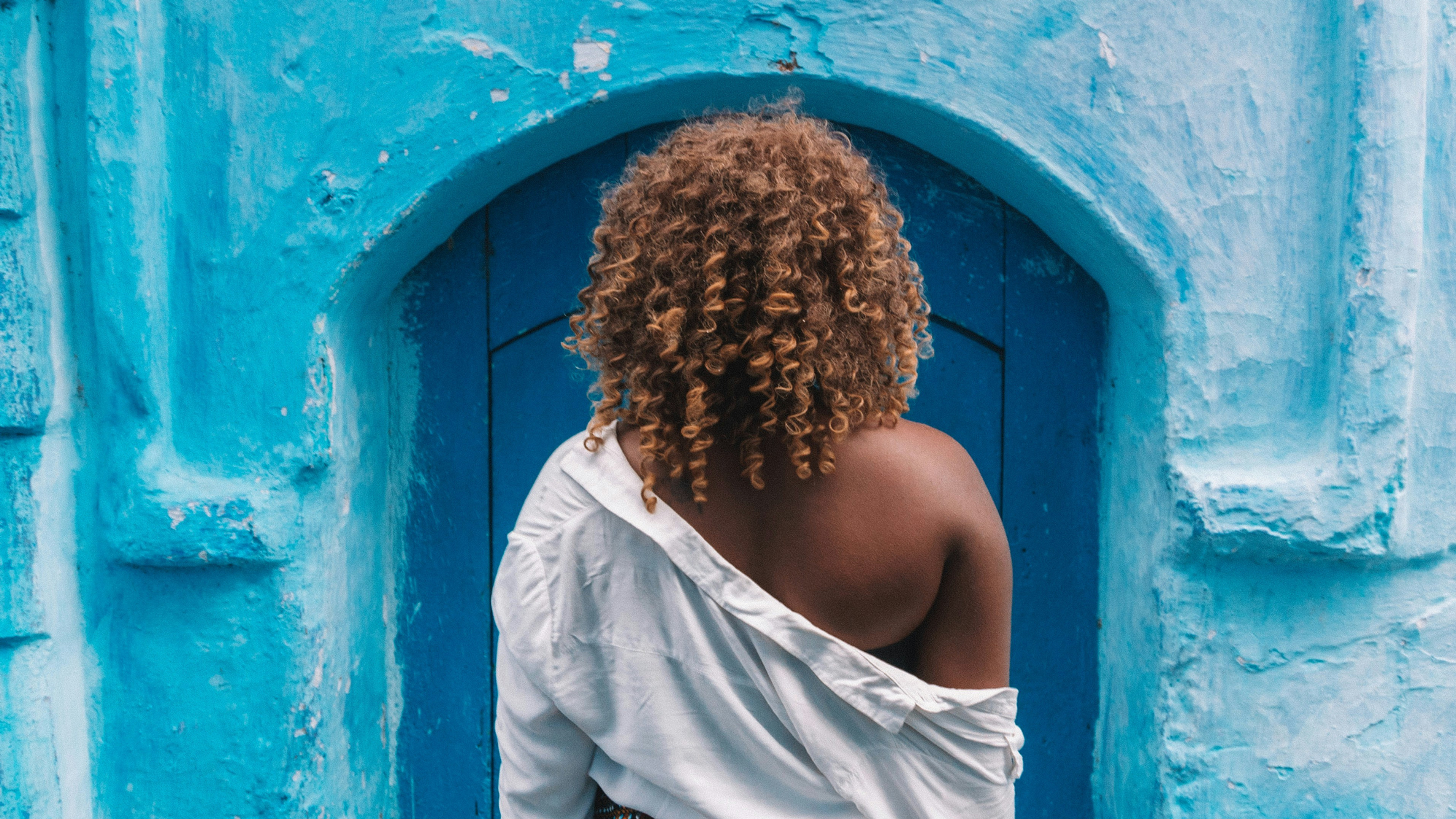 A solo traveler in white framed by a vivid blue doorway in an old-town street, the kind of fully supported solo escape Limin' Professionals plans.
