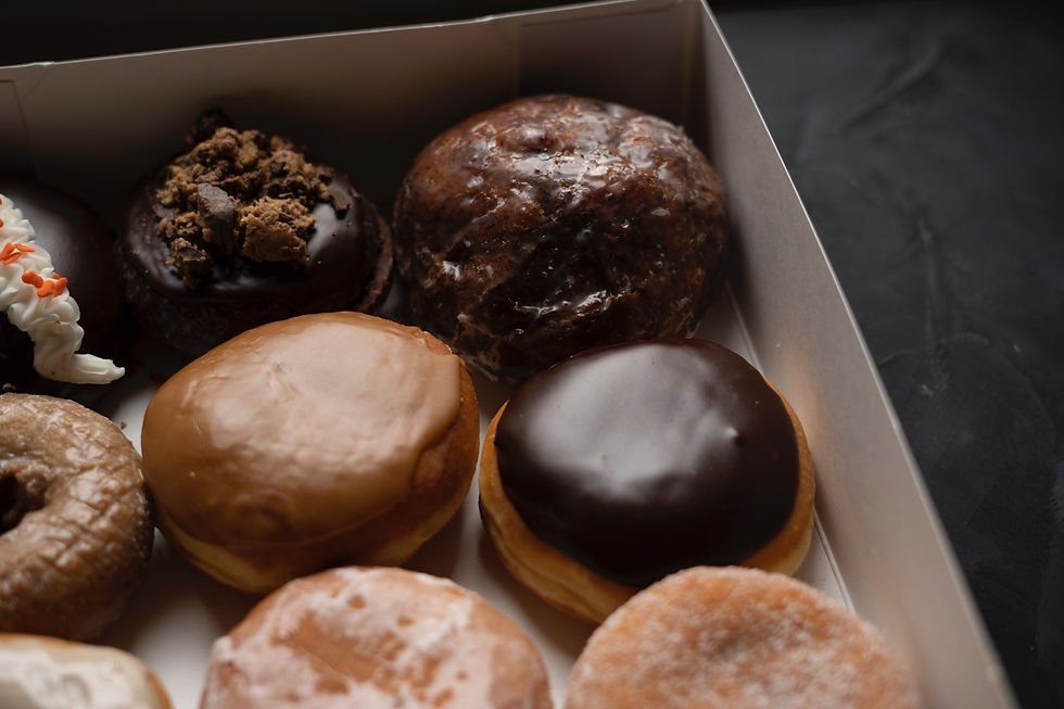 A box of assorted donuts featuring glazed, chocolate, and cream varieties with sprinkles, set on a dark surface.