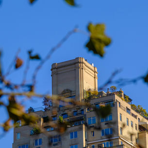 Modern Upper East Side apartment building with landscaped terraces framed by softly blurred tree branches against a clear blue sky