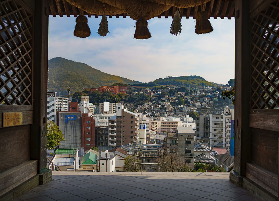 Cityscape from a wooden temple entrance, with urban buildings and lush green hills in the background under a blue sky.