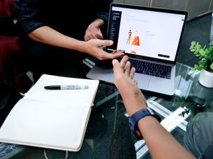 Team members collaborating at a desk where there is a notepad and an open laptop.