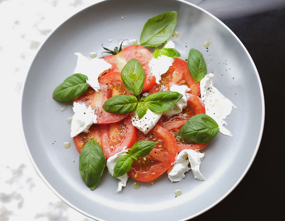Salada de tomate com queijo branco fresco e folhas de manjericão em prato cinza