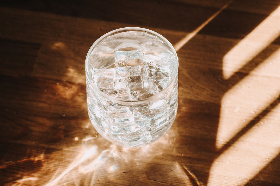 Glass of iced water on a wooden table with sunlight creating shadows and reflections. The mood is calm and refreshing. No text visible.