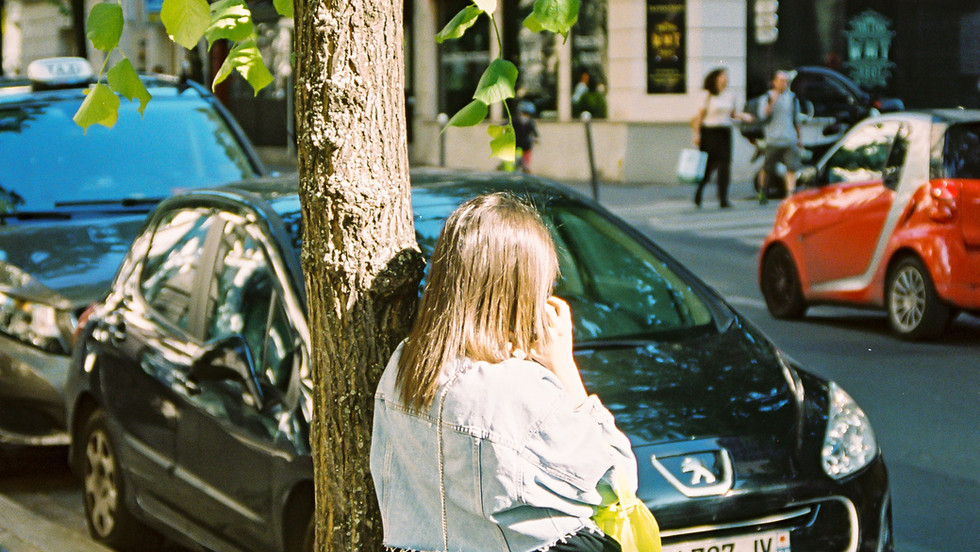 woman leaning on tree talking on the phone near a car