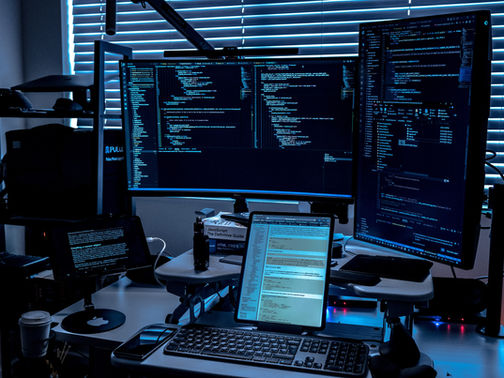 Blue-lit coding desk with three monitors showing code, tablet and keyboard